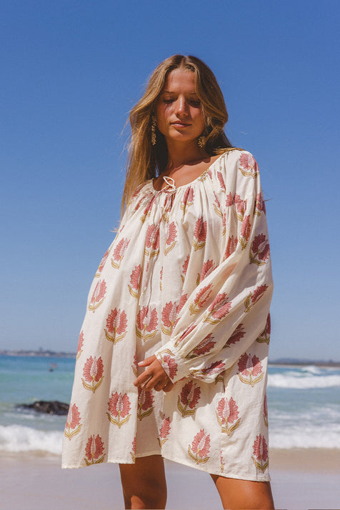 Ria Mini Dress Strawberry Cream — mid-body beach front view, model wearing strawberry cream floral hand block print cotton mini dress with ocean backdrop, relaxed A-line fit, artisan Jaipur India | Daughters of India